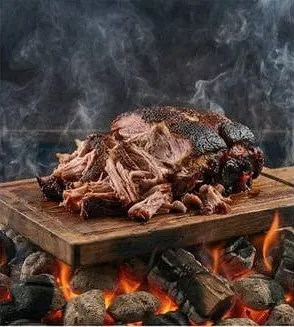 Smoked pork shoulder, pulled, on a board over coals